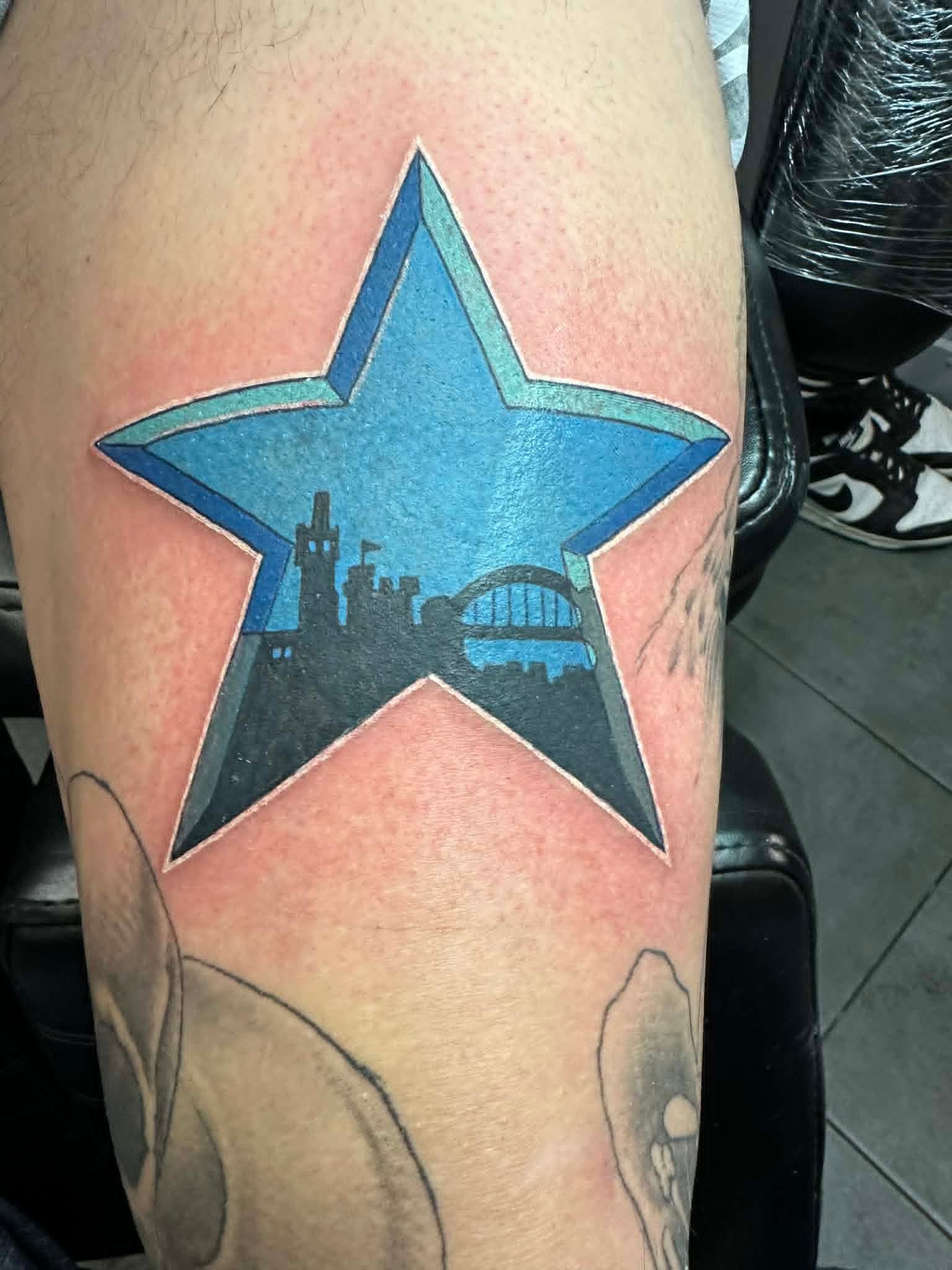Newcastle Brown Ale blue star with Tyne Bridge skyline upper arm tattoo by John Quinn at Tattoo Zone Newcastle.