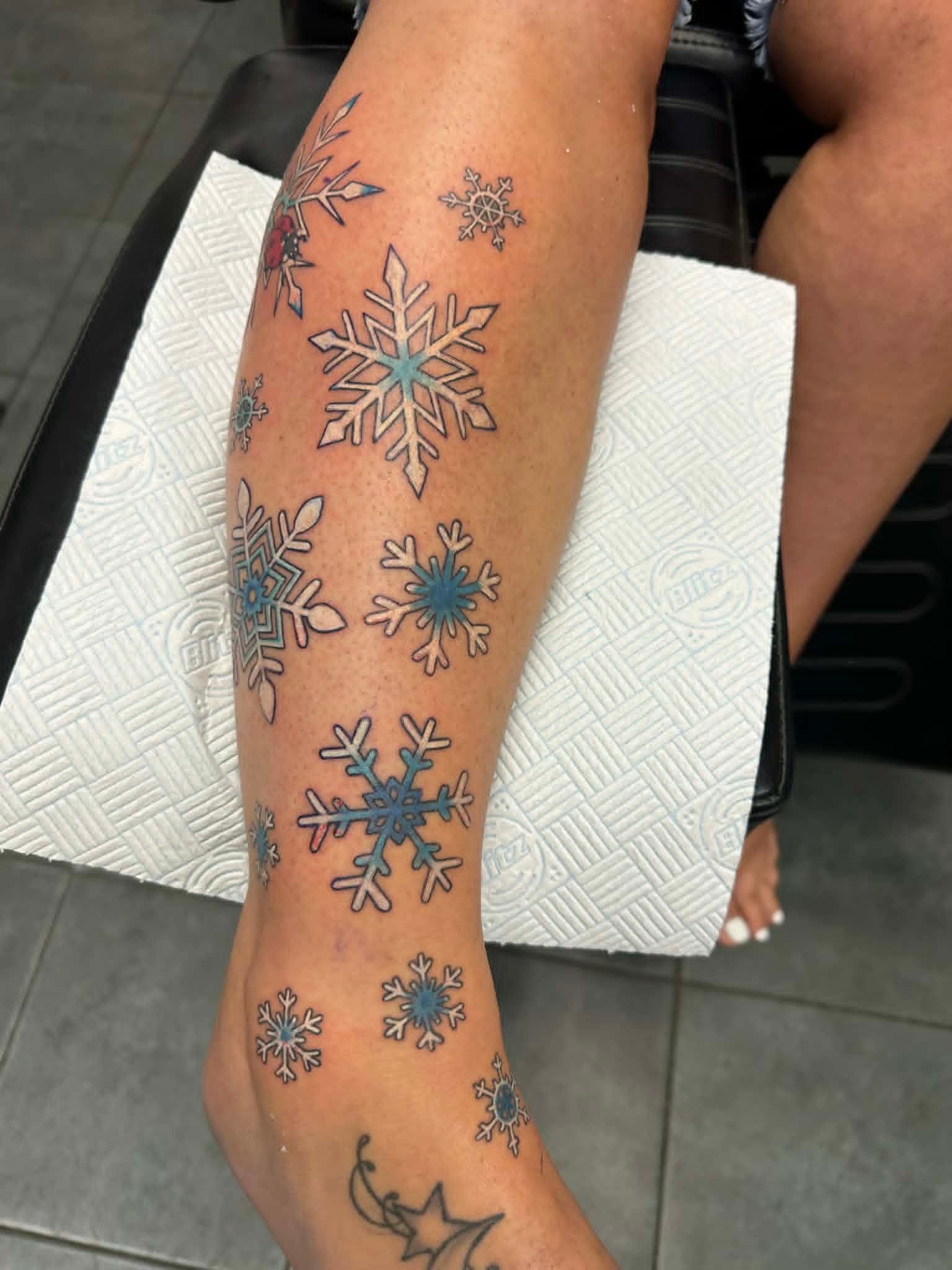 Custom scattered blue snowflakes down calf and ankle by John Quinn at Tattoo Zone Newcastle.