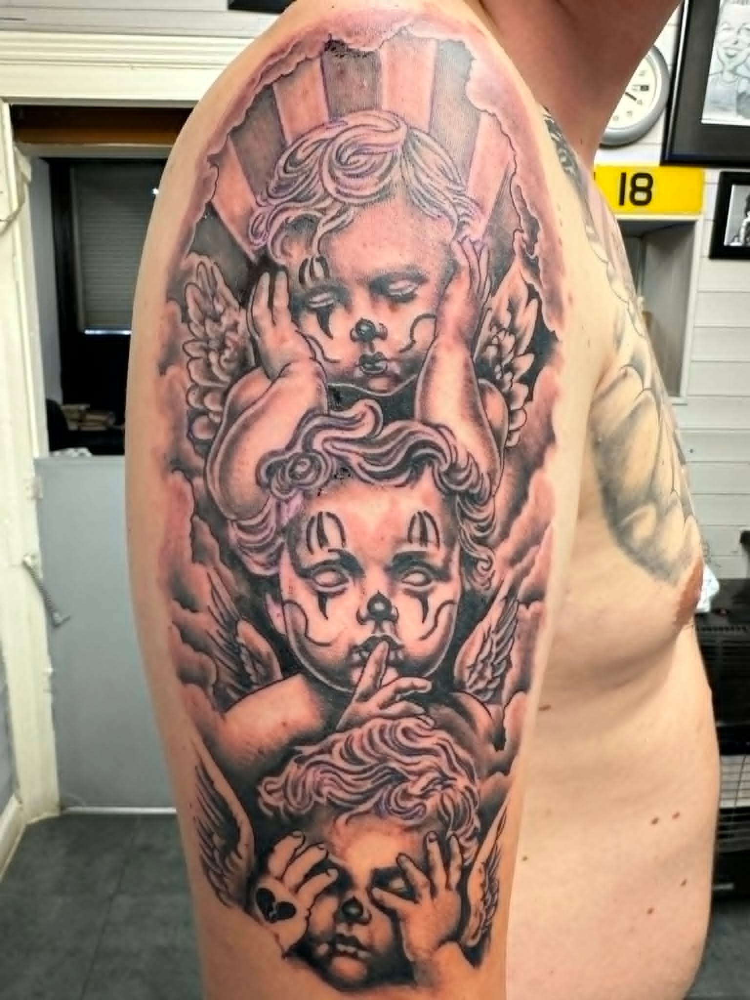 Black and grey Chicano style cherubs with clown face paint tattoo on the upper arm by John Quinn at Tattoo Zone Newcastle.