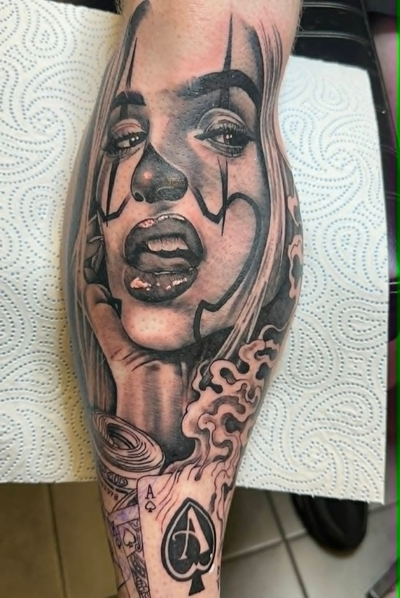 Black and grey Chicano clown girl with ace of spades calf tattoo, Chicano tattoos Newcastle by John Quinn at Tattoo Zone.
