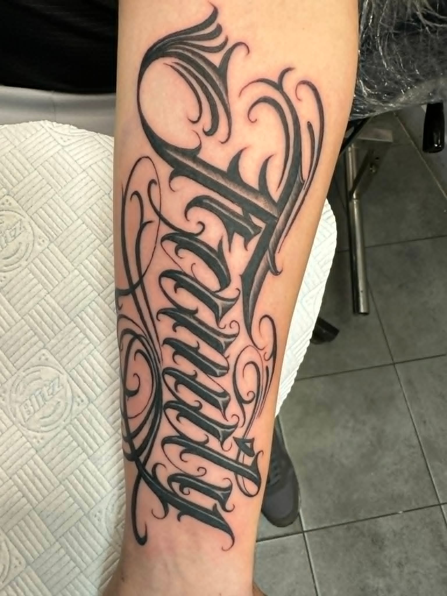 Bold Chicano style script lettering tattoo on the forearm by John Quinn at Tattoo Zone Newcastle.