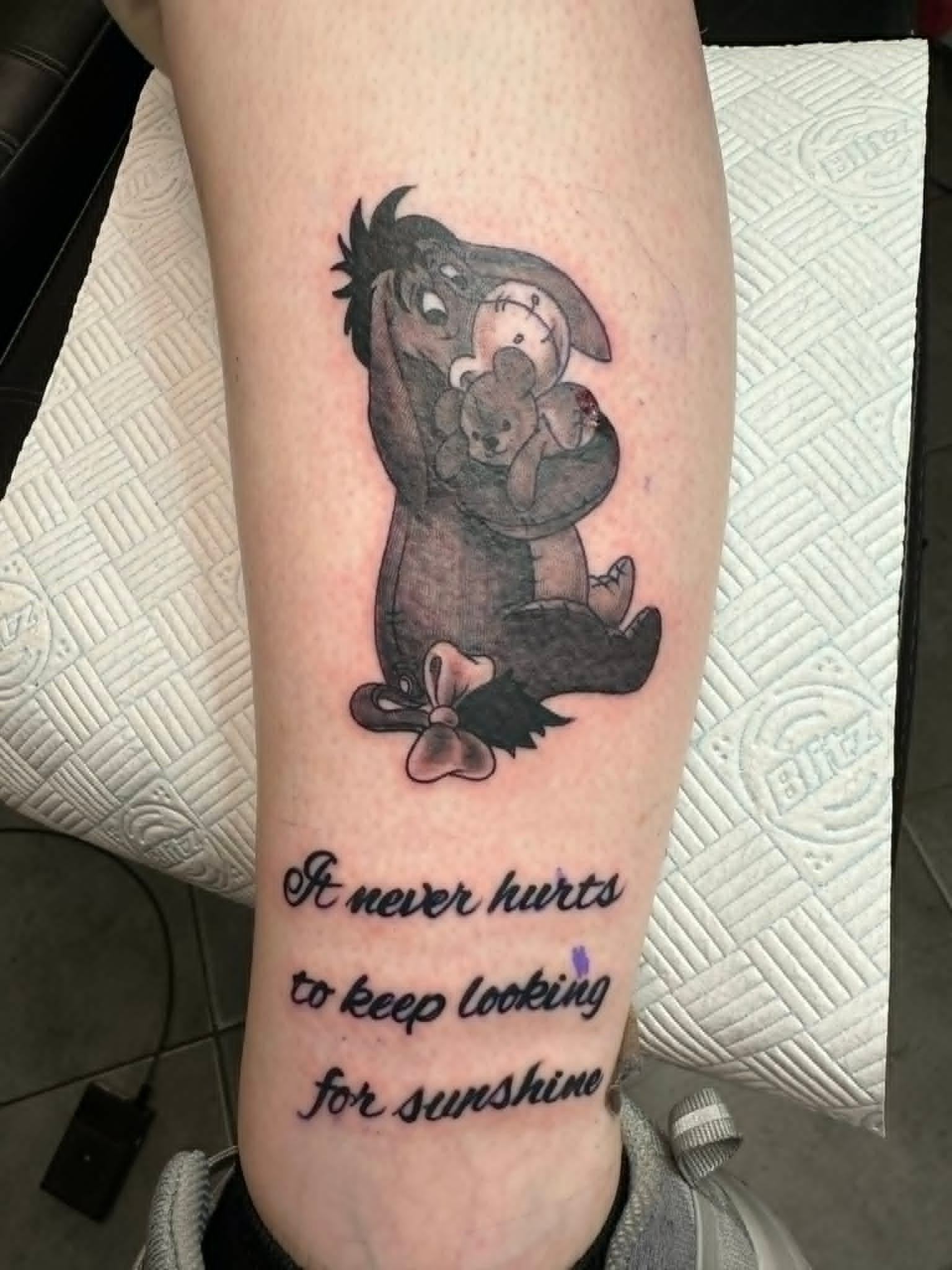 Black and grey Eeyore hugging Pooh bear with sunshine script calf tattoo by John Quinn at Tattoo Zone Newcastle.