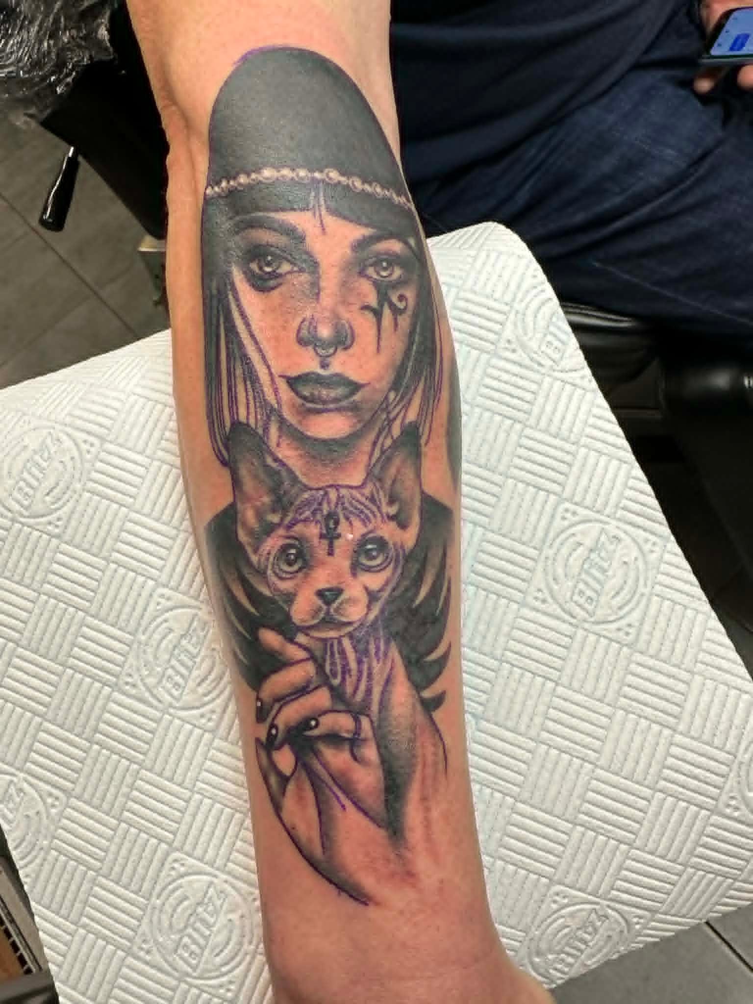Black and grey Egyptian priestess holding sphynx cat with ankh markings calf tattoo by John Quinn at Tattoo Zone Newcastle.
