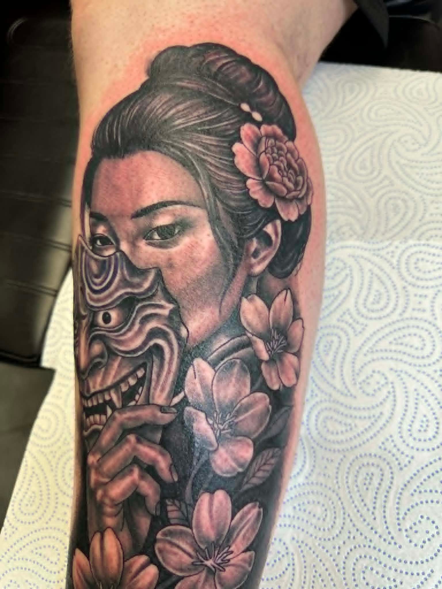 Black and grey geisha holding a hannya mask with cherry blossoms on the forearm by John Quinn at Tattoo Zone, tattoos Newcastle.