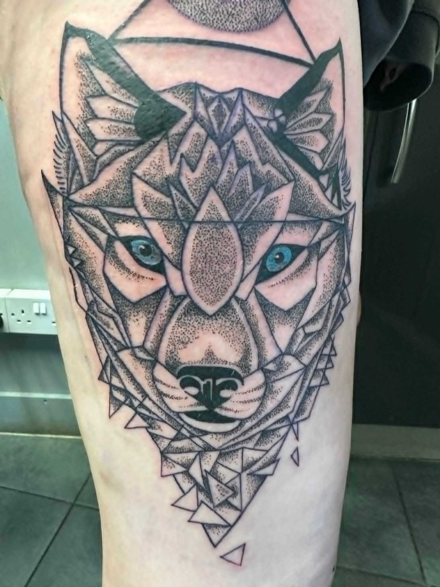 Fine line geometric dotwork wolf with blue eyes thigh tattoo by John Quinn at Tattoo Zone Newcastle.
