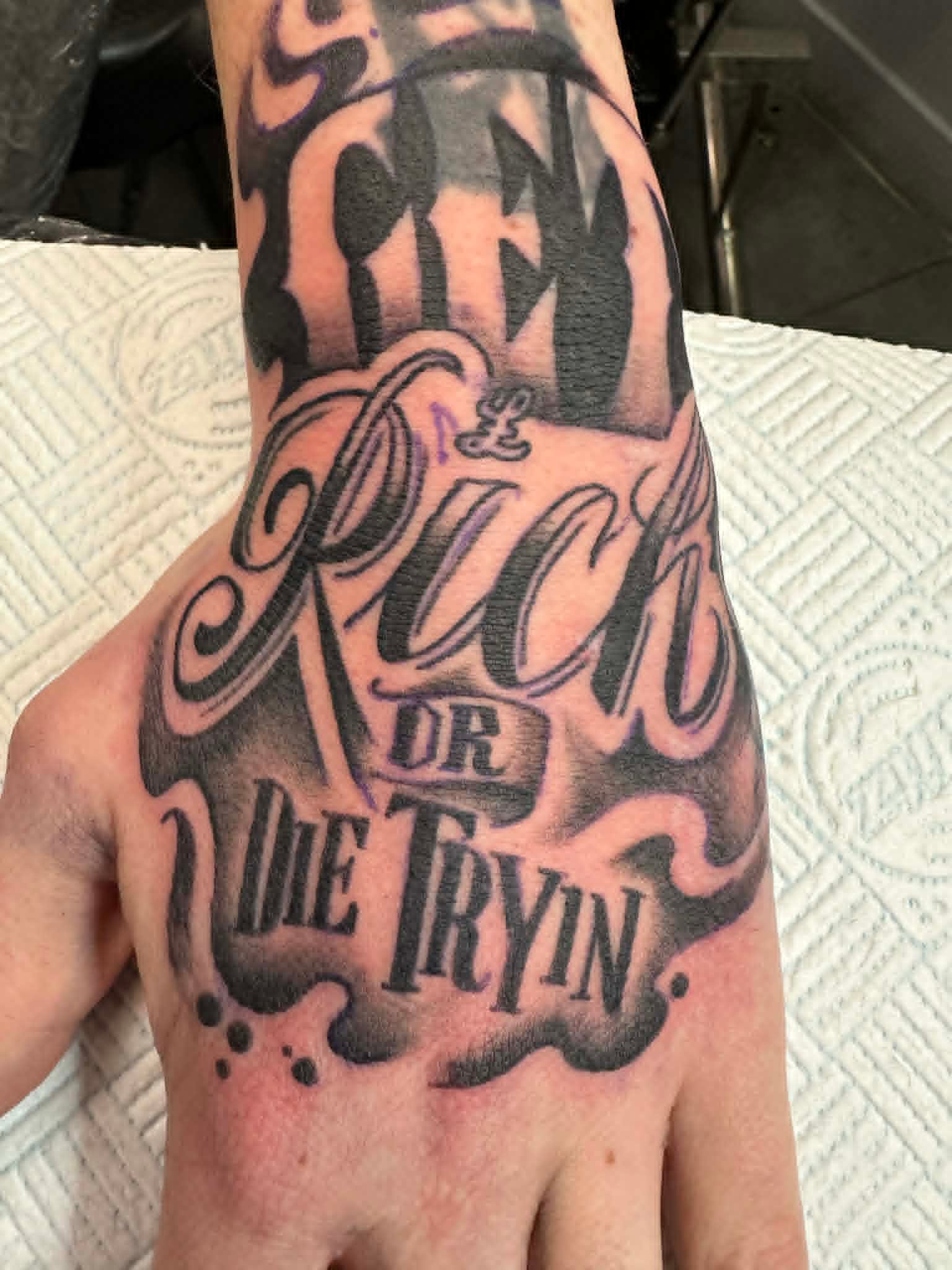 Custom chicano script lettering Get Rich or Die Tryin hand tattoo by John Quinn at Tattoo Zone Newcastle.