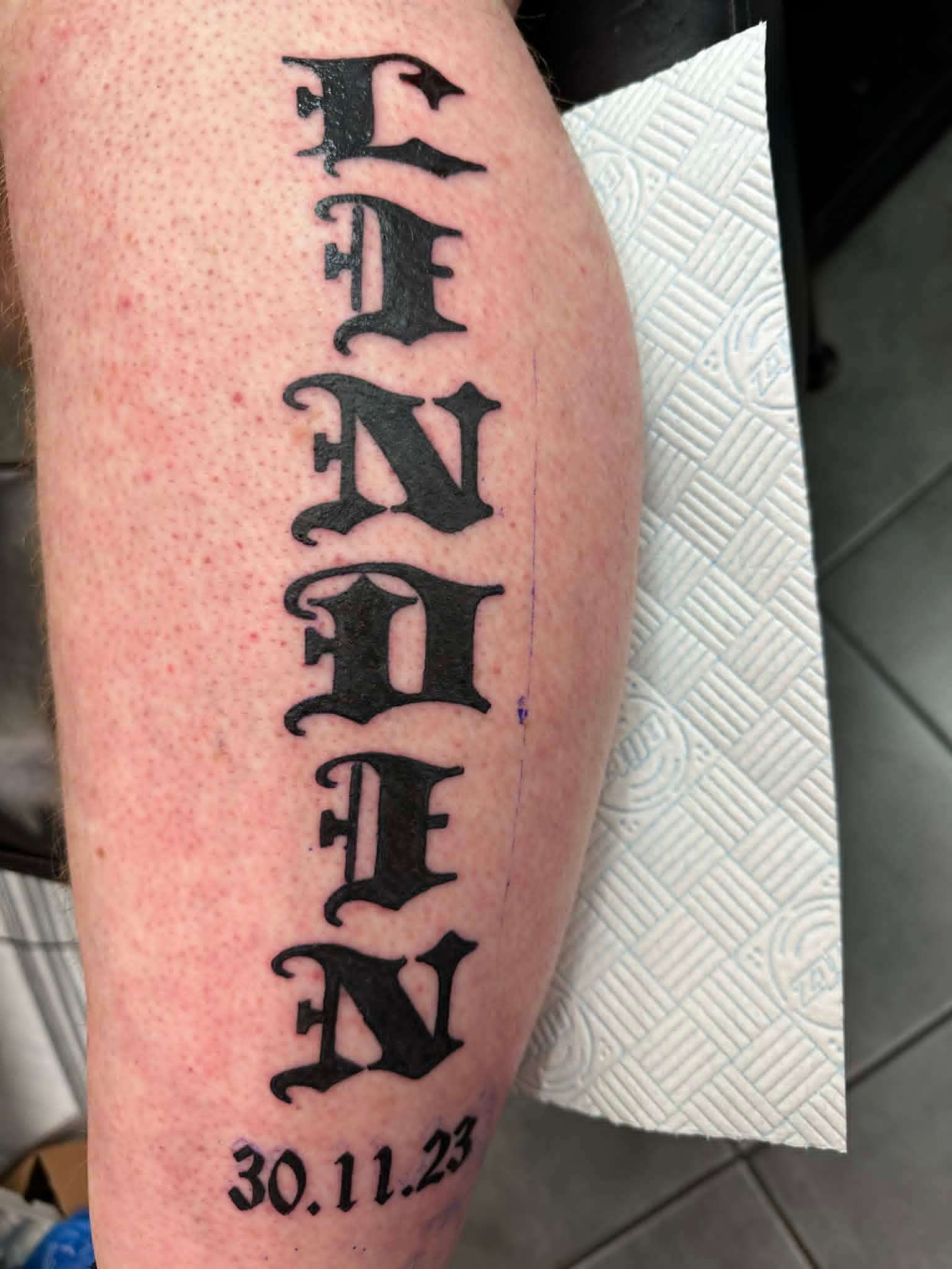 Bold gothic Linden name and date lettering calf tattoo by John Quinn at Tattoo Zone, tattoos Newcastle.