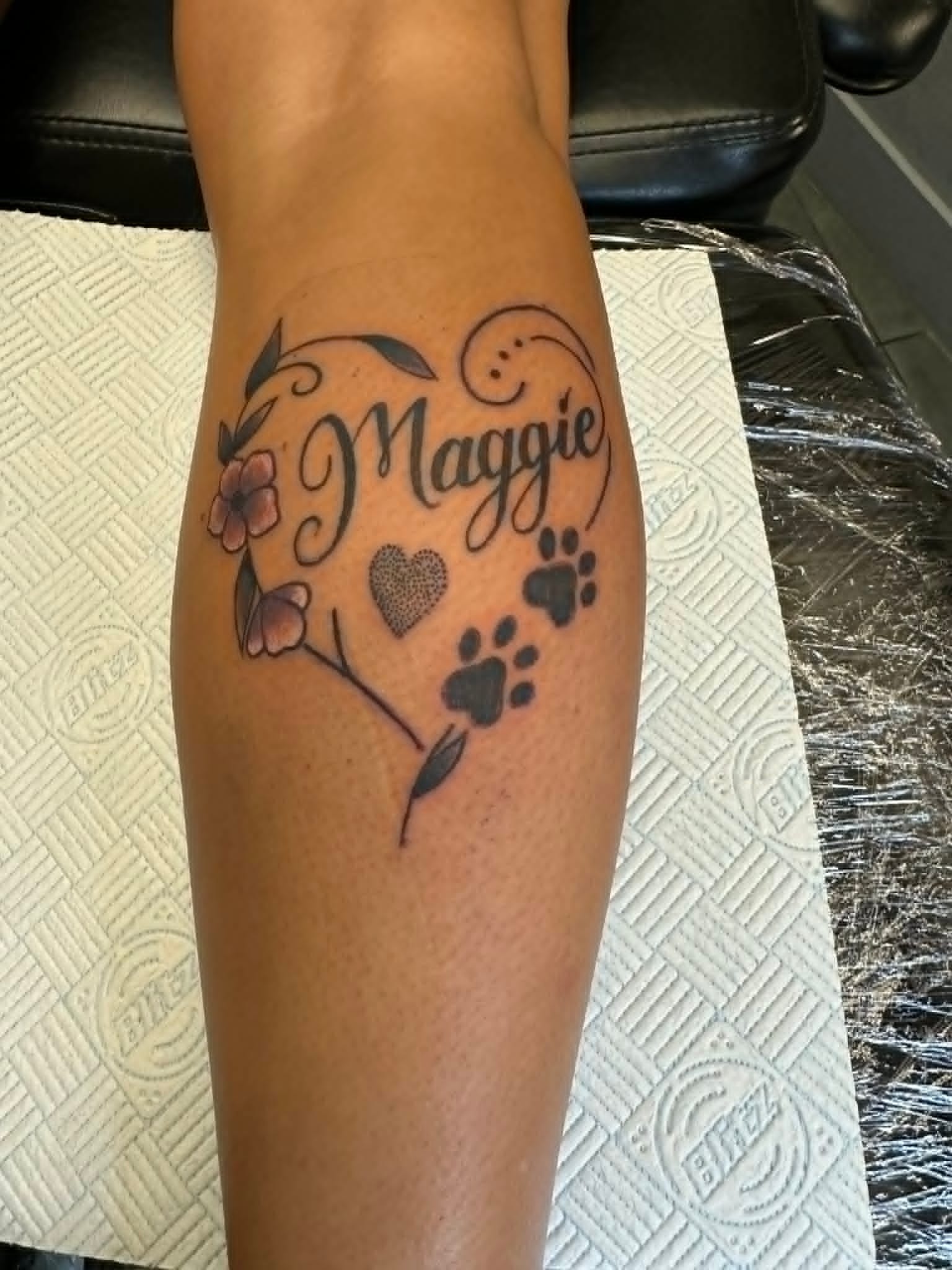 Fine line Maggie pet memorial heart with paw prints and flowers on the leg by John Quinn at Tattoo Zone, tattoos Newcastle.