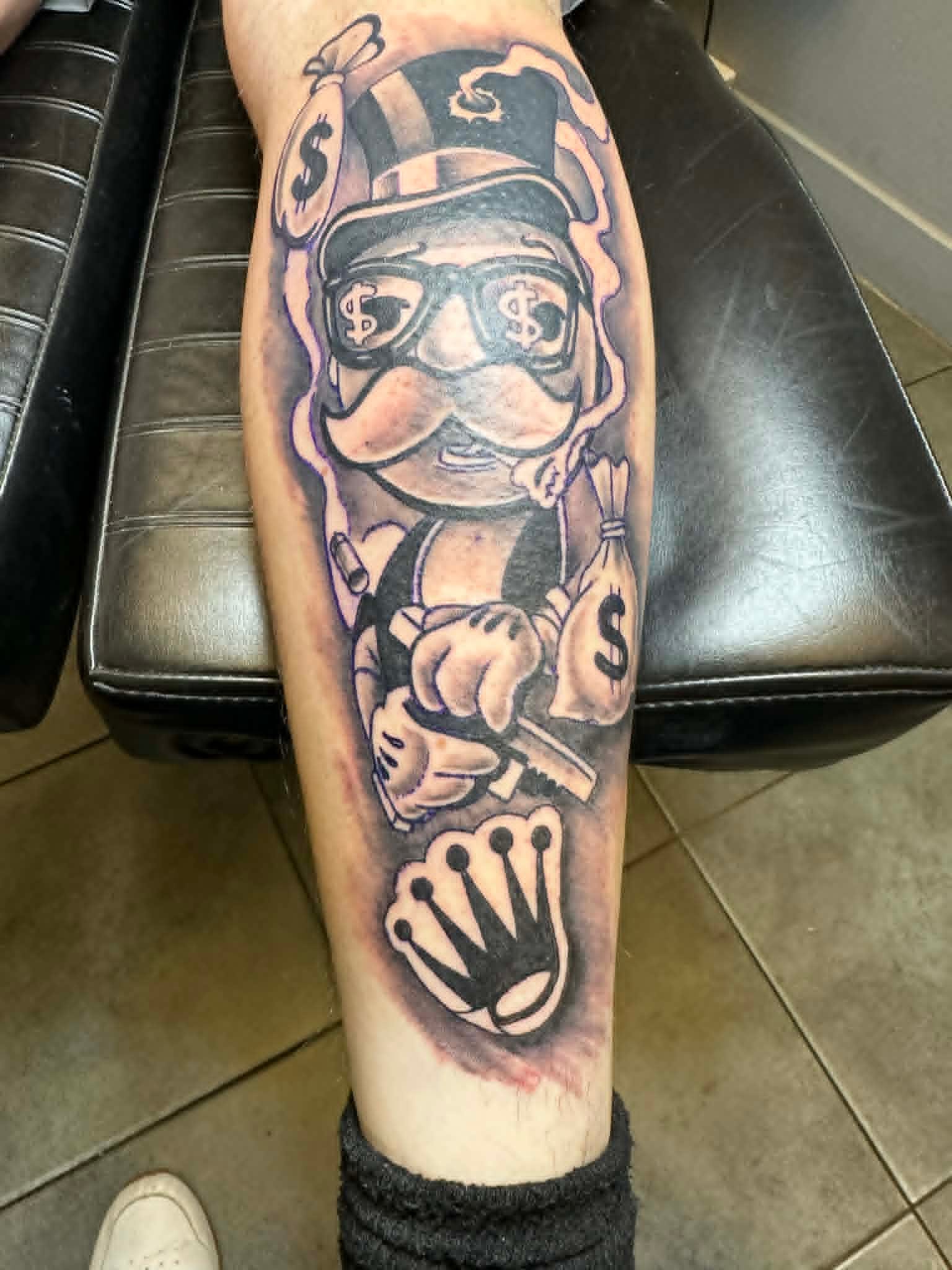 Custom Monopoly style money bag character tattoo with crown and Rolex in black and grey by John Quinn at Tattoo Zone Newcastle.