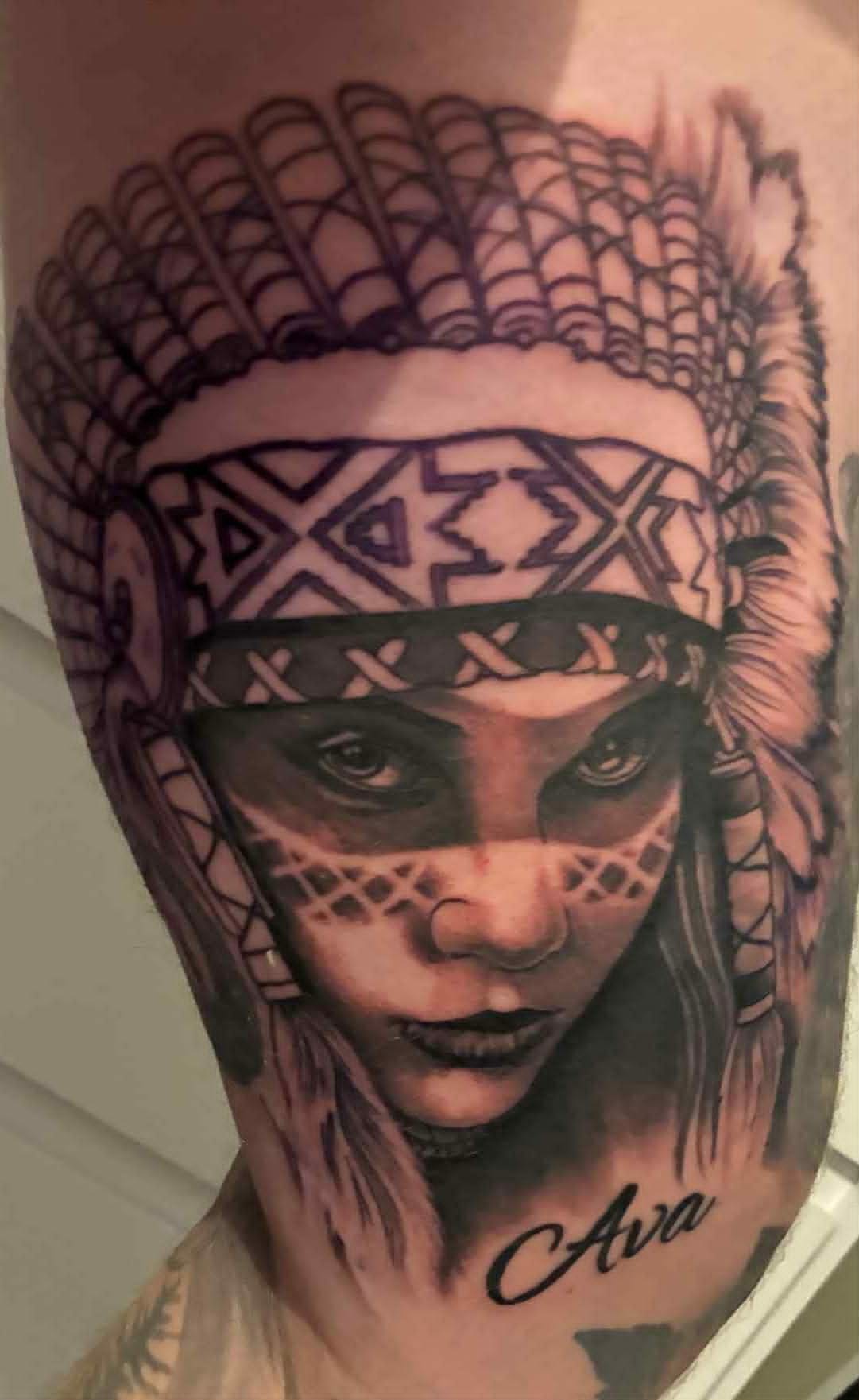 Realism Native American woman with feathered headdress and Ava cursive lettering upper arm tattoo by John Quinn at Tattoo Zone Newcastle.