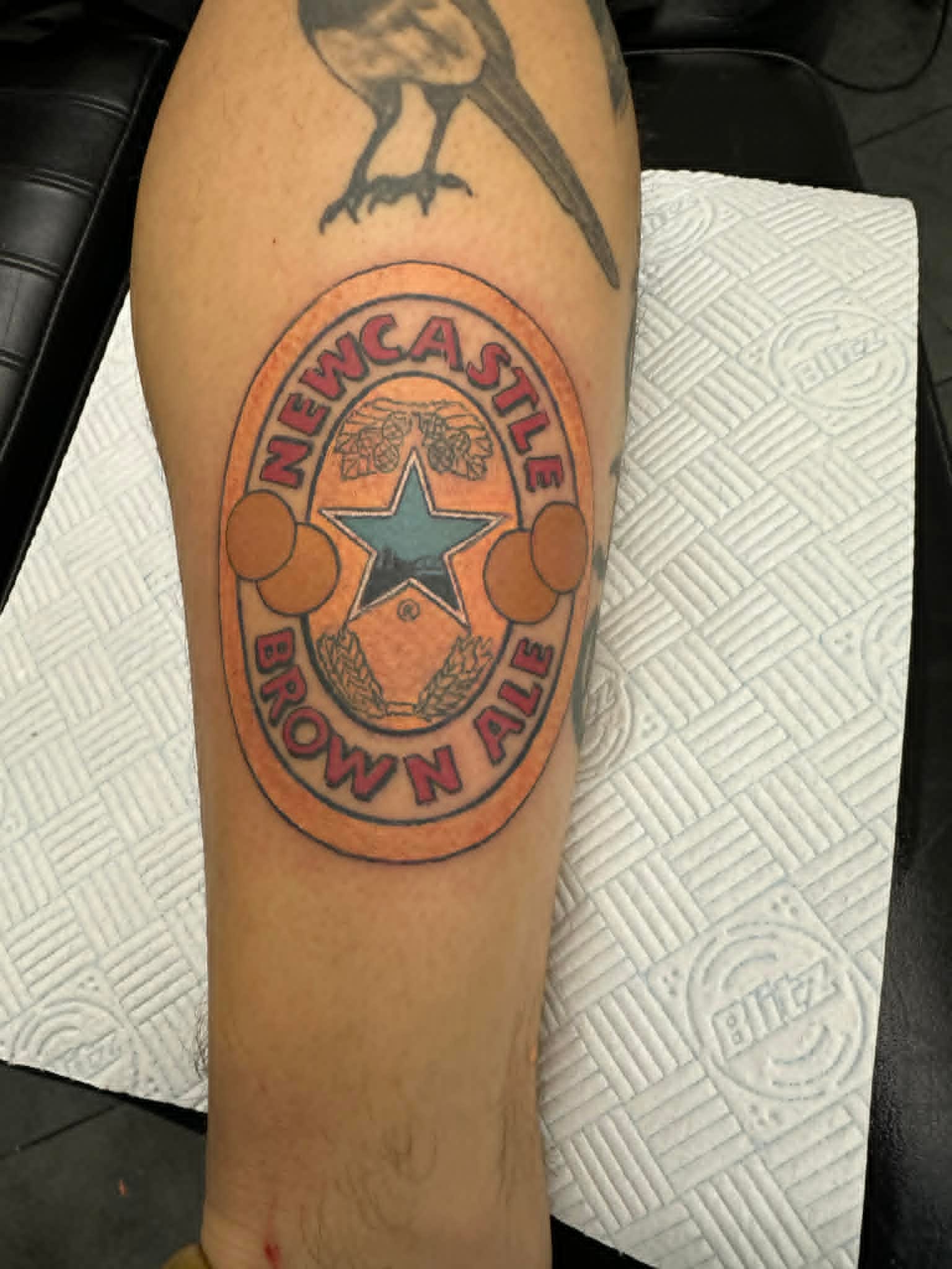 Traditional Newcastle Brown Ale label tattoo on the calf by John Quinn at Tattoo Zone, tattoos Newcastle.