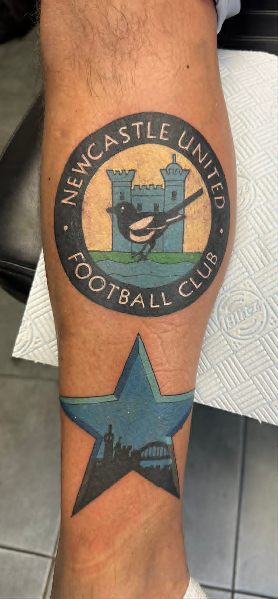 NUFC club crest with blue star and Tyne Bridge skyline on the calf by John Quinn at Tattoo Zone, tattoos Newcastle.