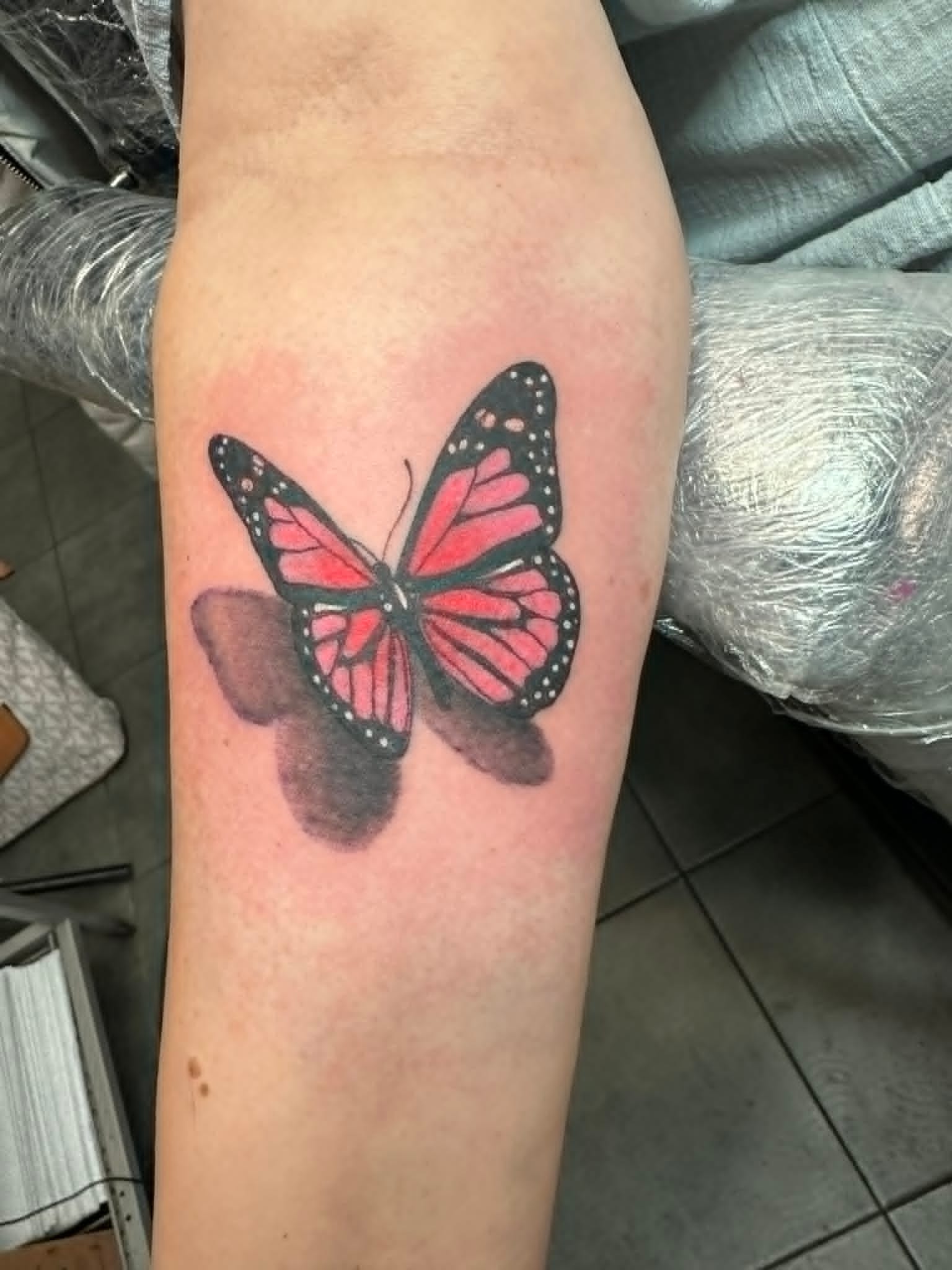 Custom pink and red monarch butterfly with soft shadow forearm tattoo by John Quinn at Tattoo Zone Newcastle.