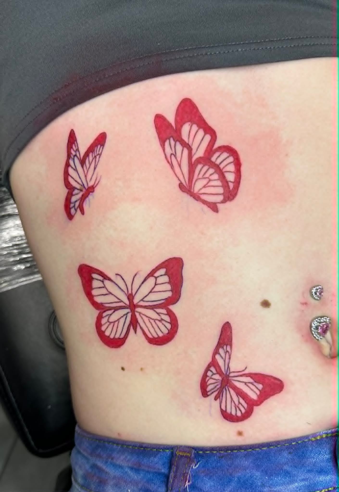 Fine line cluster of four red butterflies on ribs by John Quinn at Tattoo Zone Newcastle.