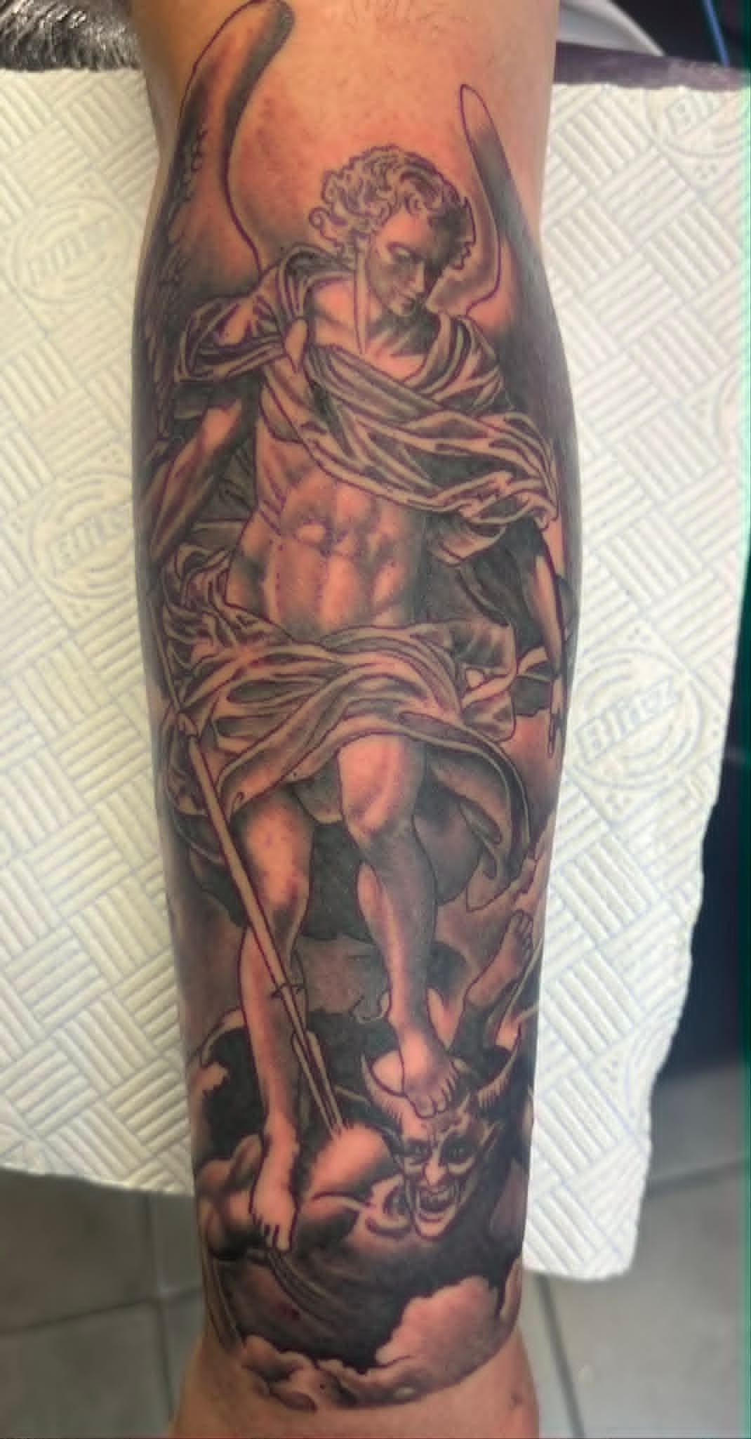 Black and grey Saint Michael archangel defeating devil forearm tattoo by John Quinn at Tattoo Zone, tattoos Newcastle.