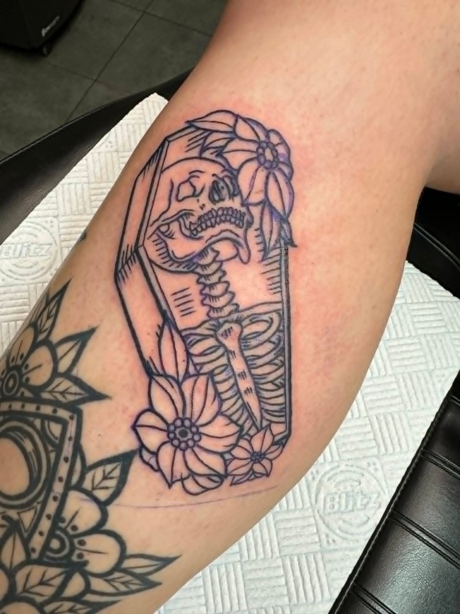 Traditional outline skeleton in coffin with flowers on inner arm by John Quinn at Tattoo Zone, tattoos Newcastle.