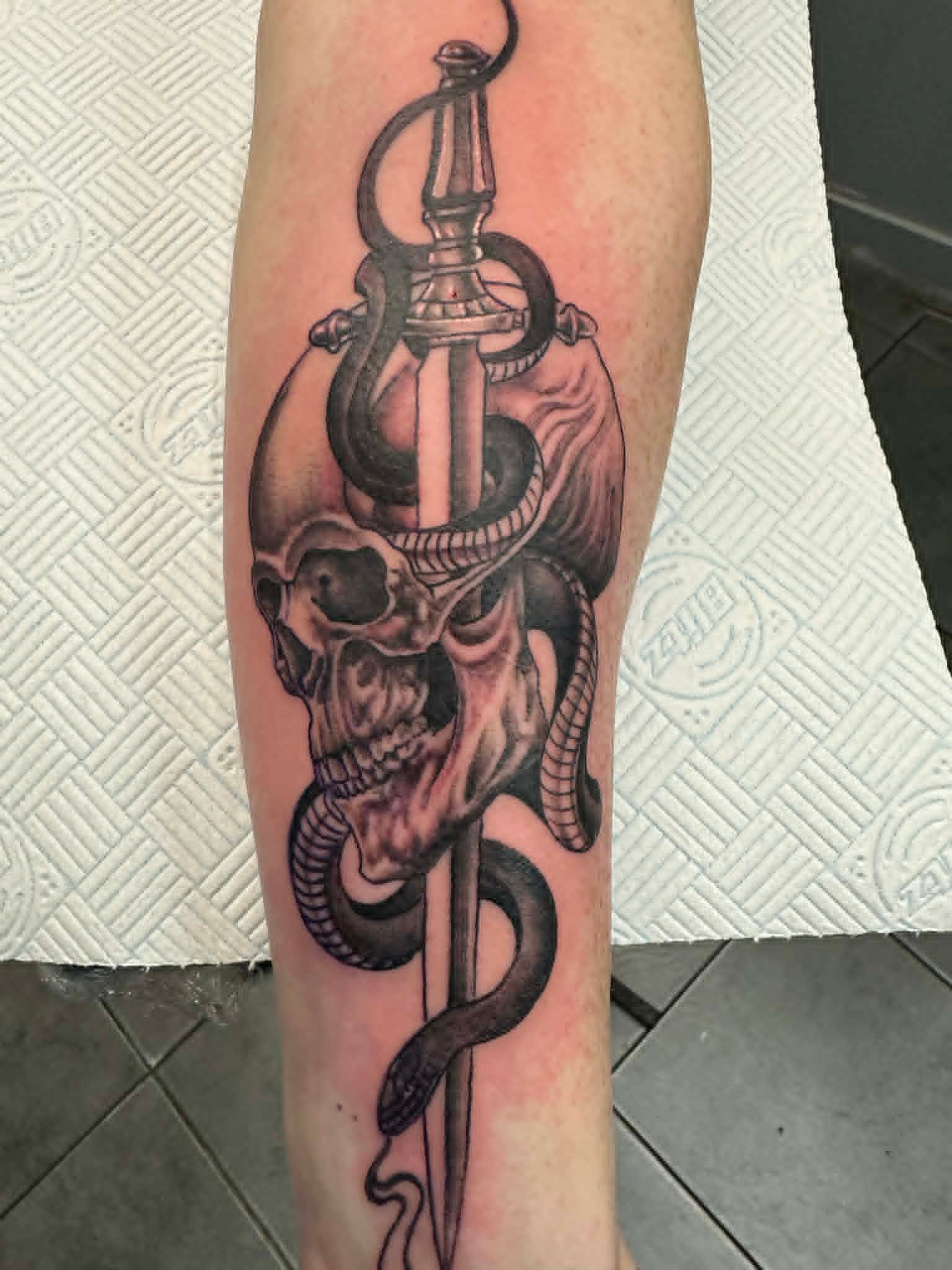 Black and grey skull pierced by sword with snake coiled around blade forearm tattoo by John Quinn at Tattoo Zone Newcastle.