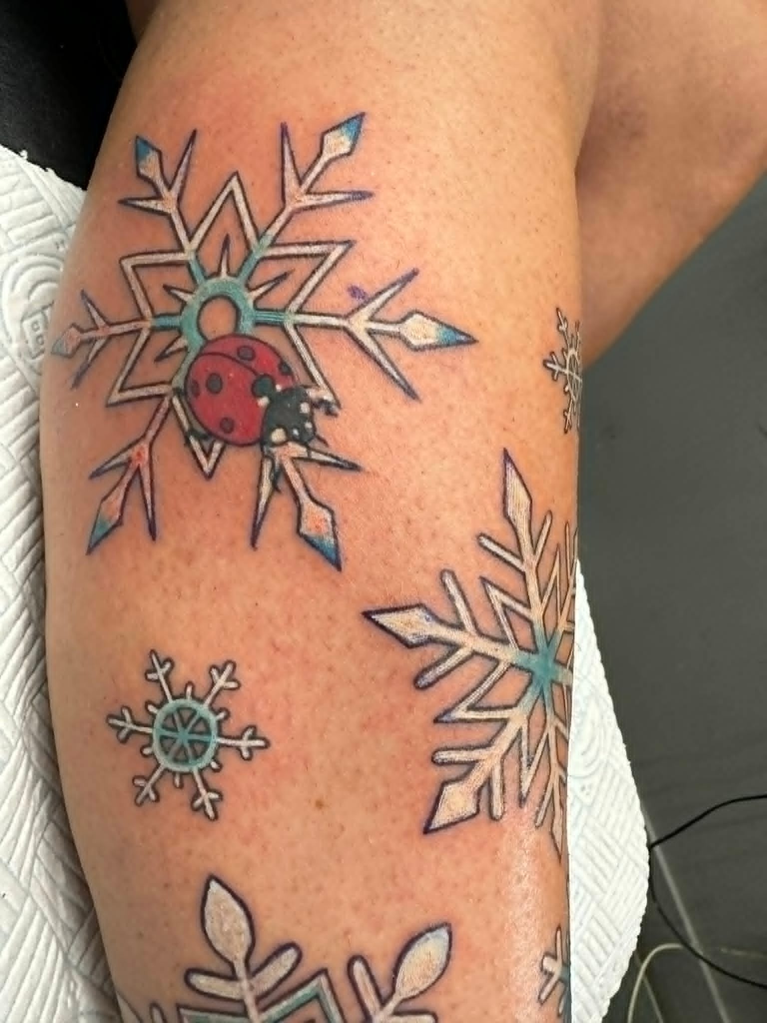 Custom colour snowflakes with ladybird tattoo on the arm by John Quinn at Tattoo Zone, tattoos Newcastle.