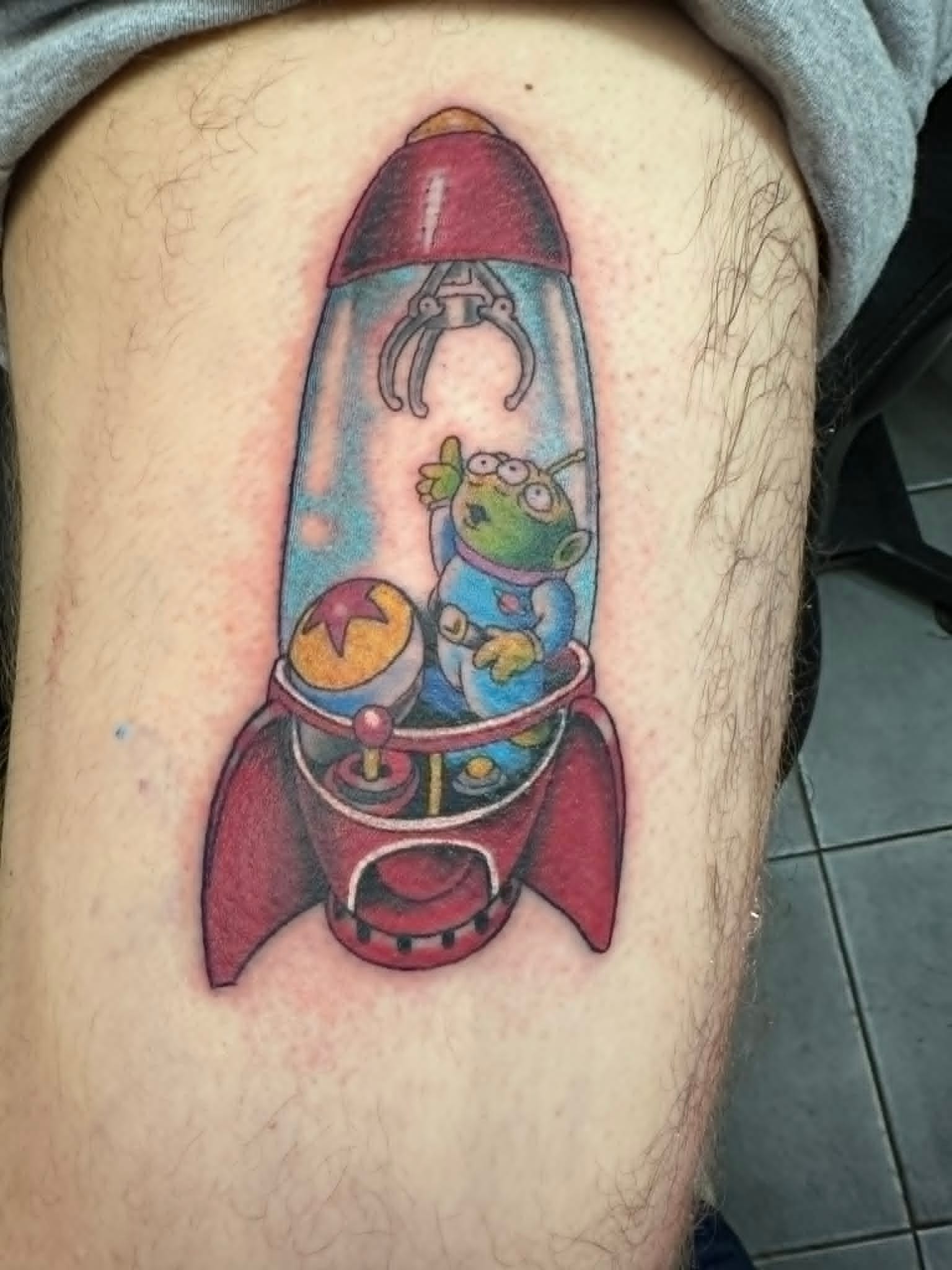 Toy Story alien inside red rocket ship custom colour tattoo on thigh by John Quinn at Tattoo Zone, tattoos Newcastle.