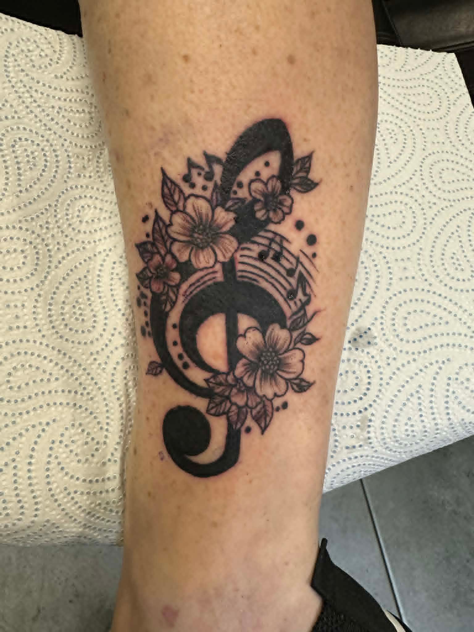 Black and grey treble clef with flowers on leg by John Quinn at Tattoo Zone, tattoos Newcastle.