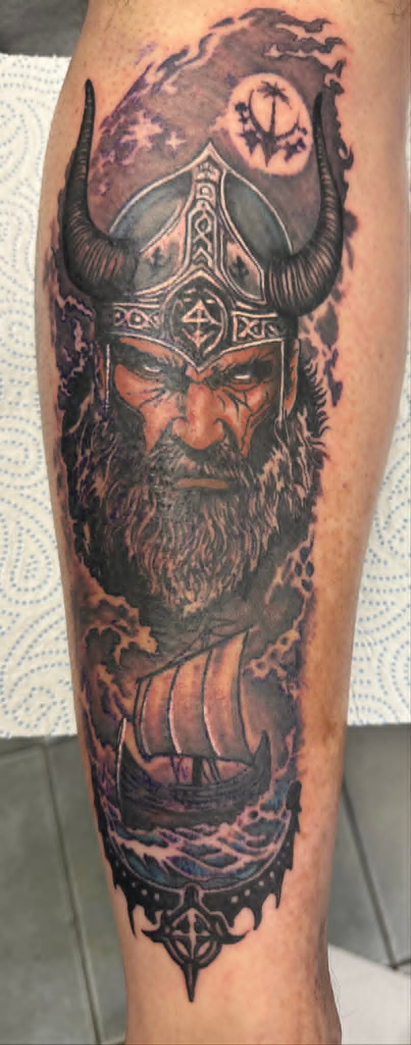 Black and grey Viking warrior with horned helmet, longship and runes calf tattoo by John Quinn at Tattoo Zone Newcastle.
