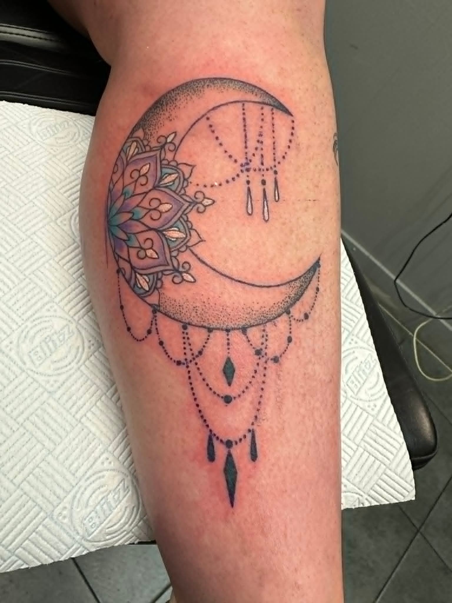 Fine line dotwork crescent moon with mandala lotus and beaded jewellery droplets calf tattoo by John Quinn at Tattoo Zone Newcastle.