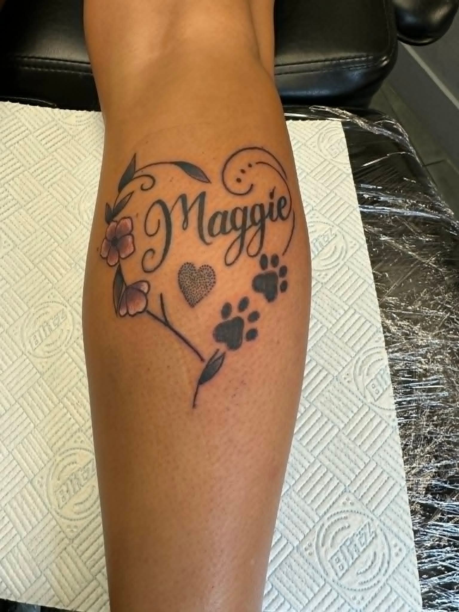 Fine line Maggie pet memorial heart with paw prints and flowers on the leg by John Quinn at Tattoo Zone, tattoos Newcastle.